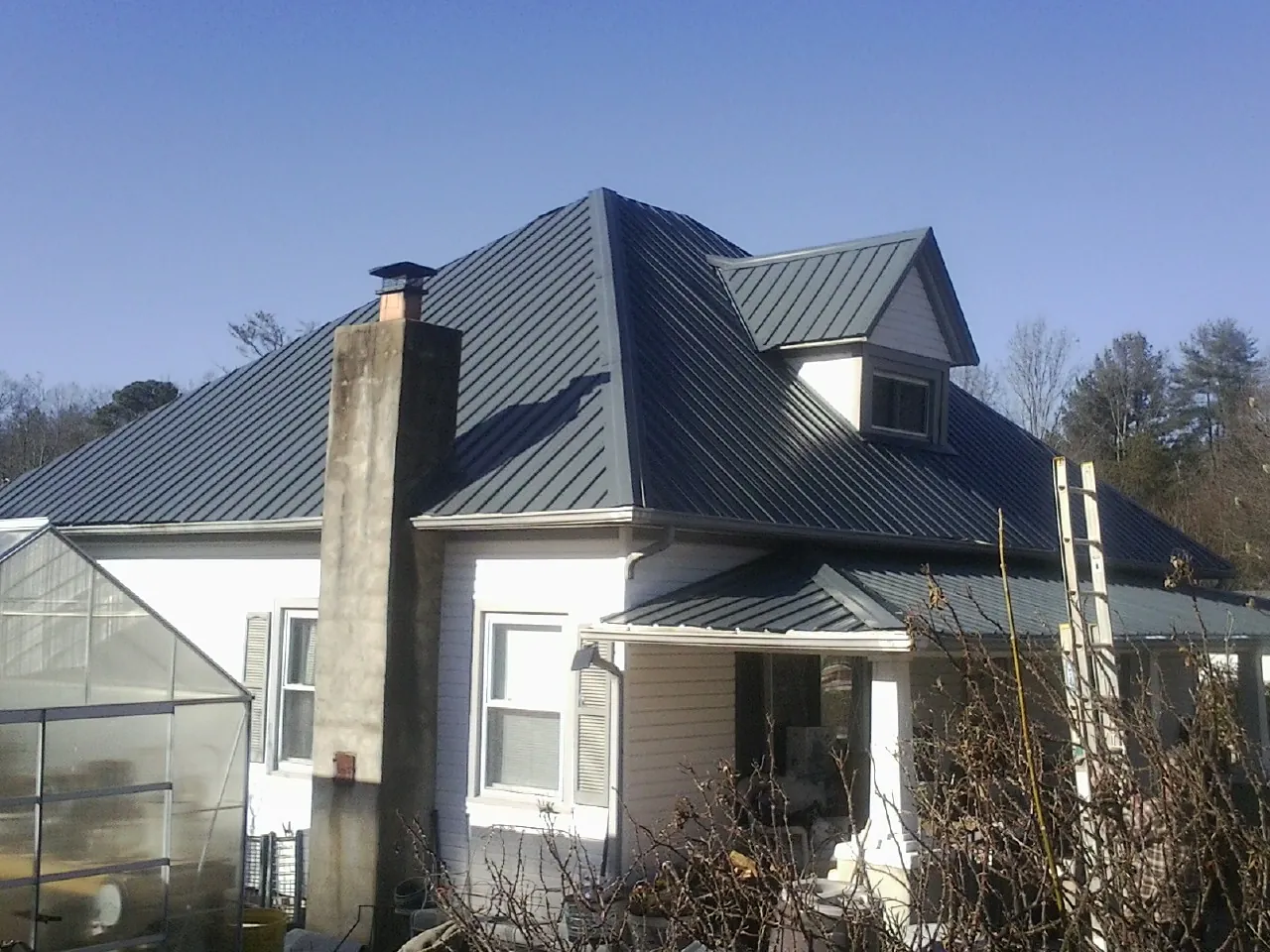 Dark blue standing seam metal roof on a white farmhouse with dormer — Slate & Tile Roof Repair by Roofing Brothers in Oshkosh