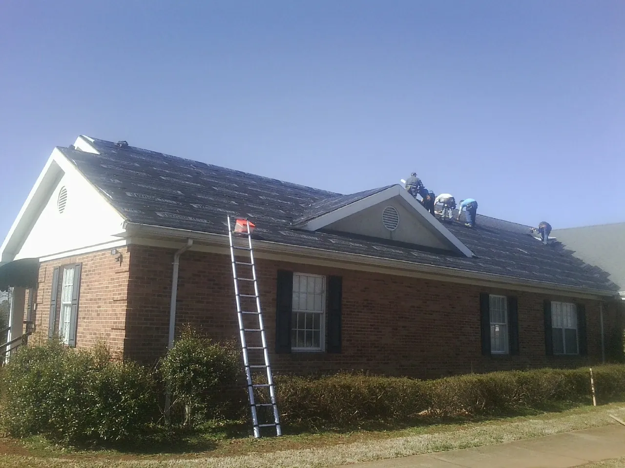 Crew tearing shingles off a brick ranch roof with a ladder set — Metal Roof Repair work by our crew in Oshkosh
