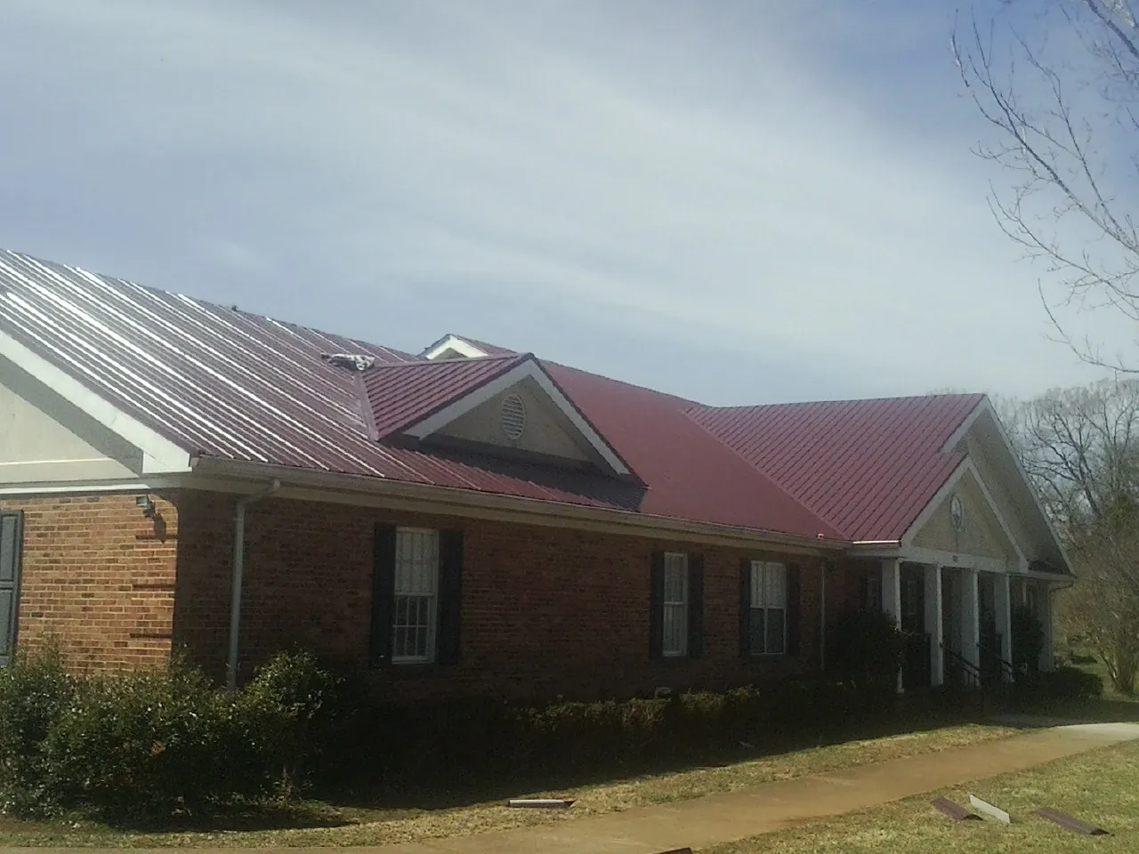 Red metal roof with gabled entries on a long brick building, from a Hail Damage Roof Repair job in Oshkosh