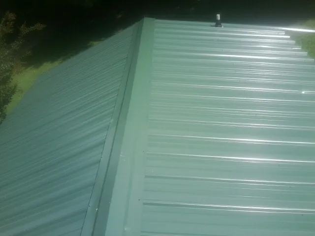 New green metal panels meeting at the ridge of a roof — Flat Roof Repair work by our crew in Oshkosh