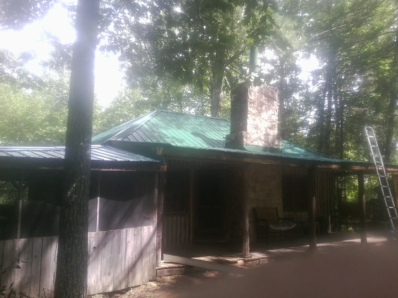 Green metal roof and stone chimney above a log cabin porch in Oshkosh