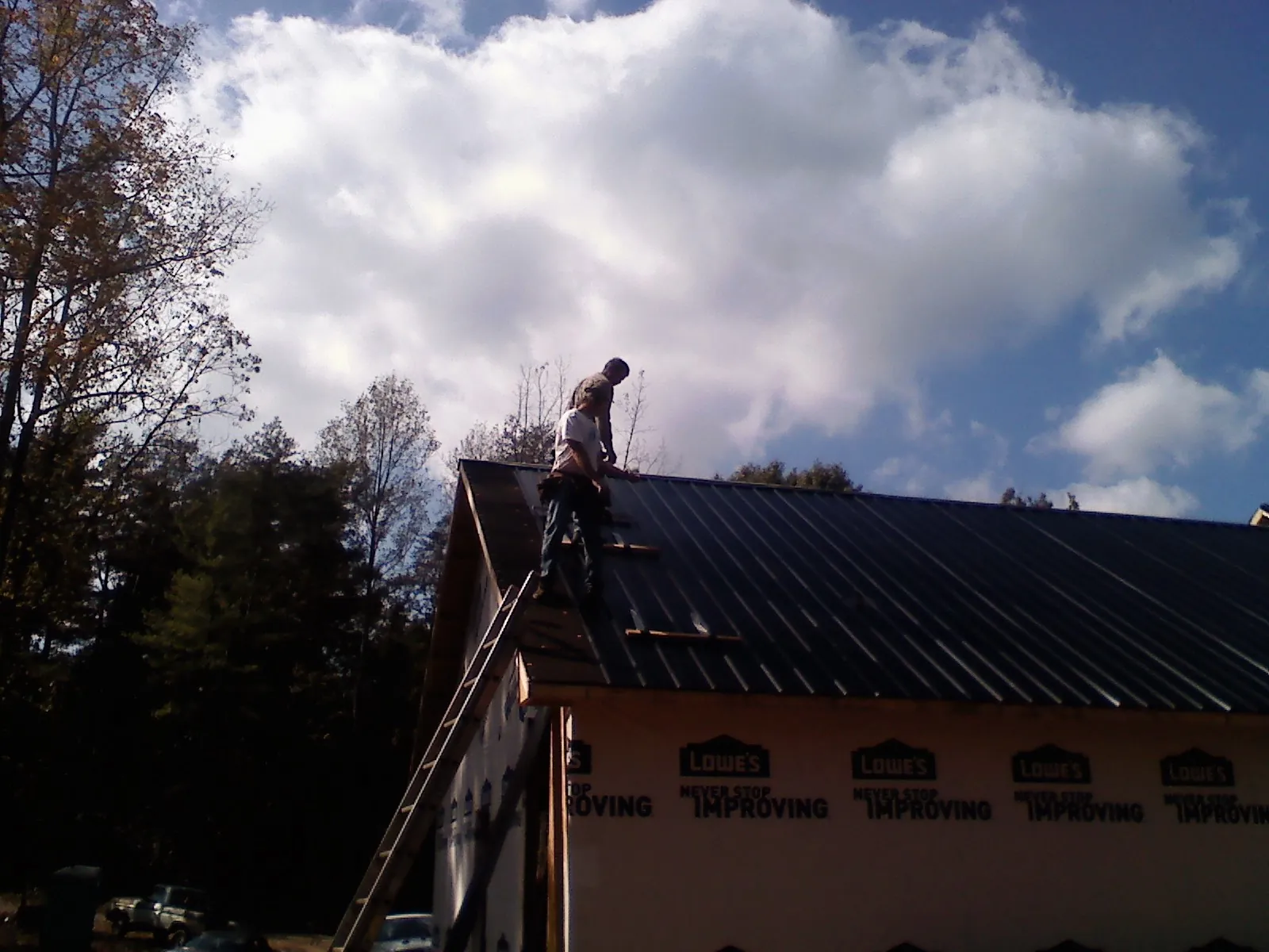 Roofer fastening dark metal panels high against a cloudy sky, from a Roof Inspection job in Oshkosh
