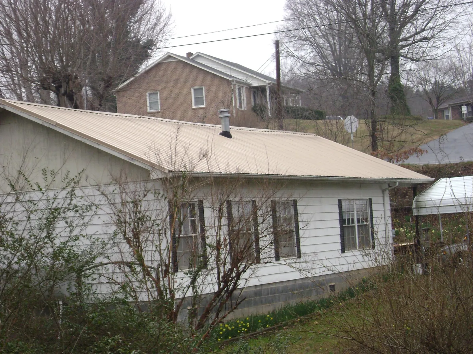 Tan metal roof on a white sided house set into a hillside — Commercial Roofing by Roofing Brothers in Oshkosh