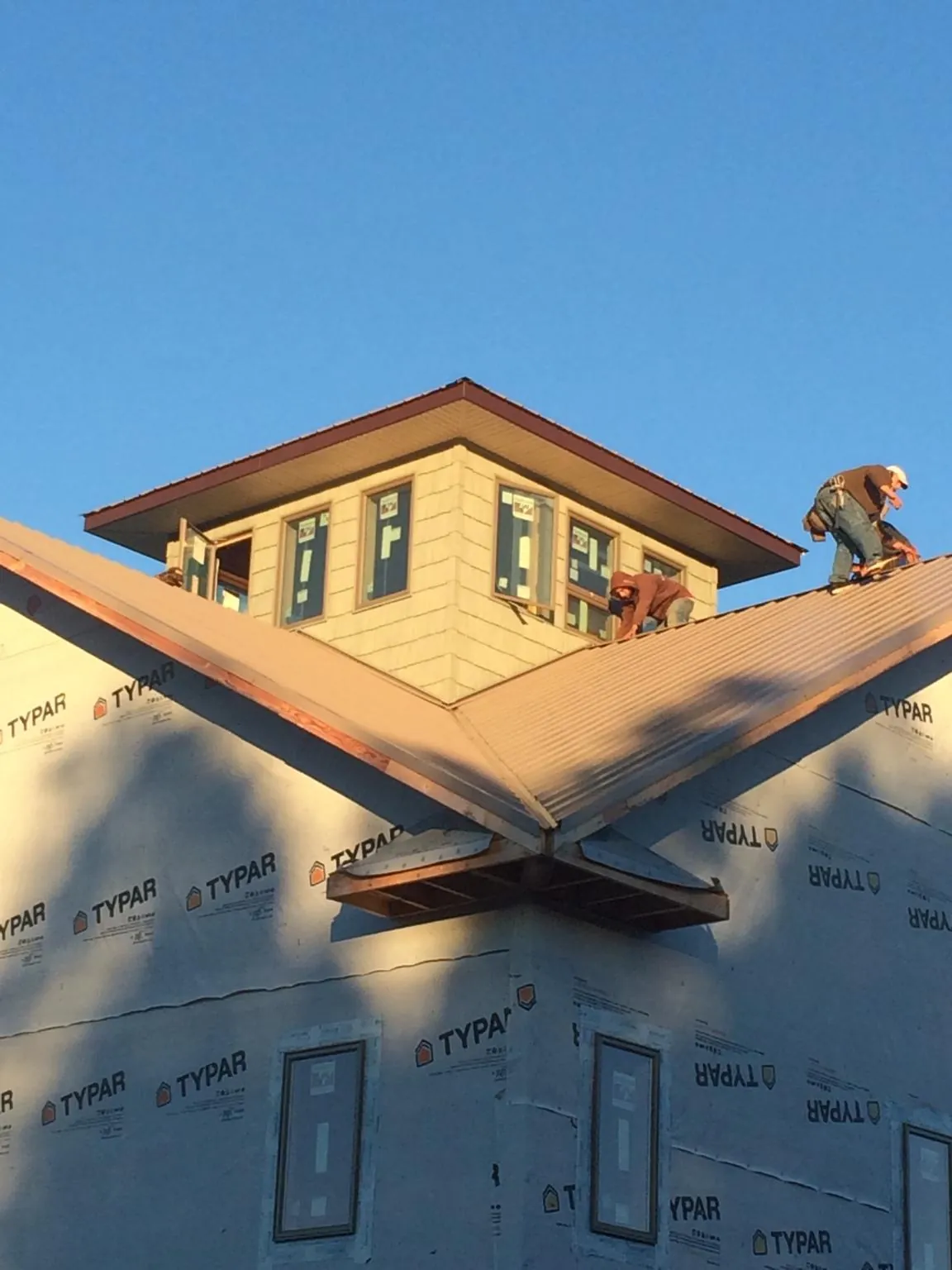 Roofers working around a rooftop cupola on a new metal roof at sunset — Roof Waterproofing in Oshkosh by Roofing Brothers